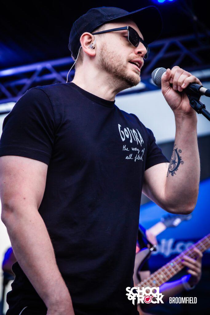 Isaac on stage at School of Rock Broomfield, mic in hand, wearing a Gojira shirt